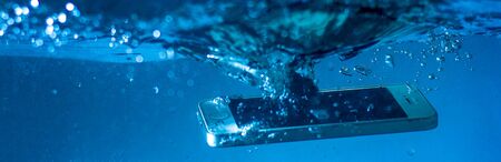 black and white phone dropped into the water. phone in water. blue water. phone in water bubbles.phone sinks in waterの写真素材