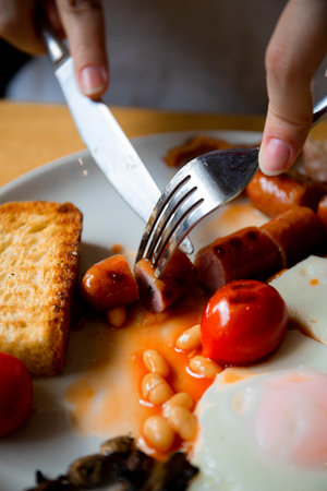 a girl with a knife and fork eats an English breakfast fresh tomatoes scrambled eggs fried eggs with rye white fresh bread and meat sausage pork sausage meat food tomorrow lunch meal healthの写真素材