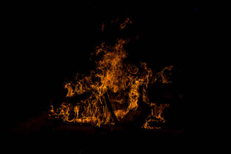 bright orange languages of a fire on wooden logs at night. wood on fire. bonfire at night. campfire. beautiful flame on black background. fire on black background. burning wood. beautiful fire texture. the texture of the campfireの写真素材
