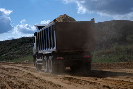Dump truck transports sand in open pit mine. Excavator on the development of sand in a quarry....