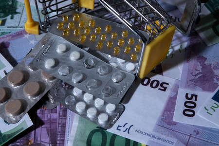 a cart from a supermarket store on a background of money. there are pills and medicine in the cart. small cart abstract background texture background of a billboard or poster dayの写真素材