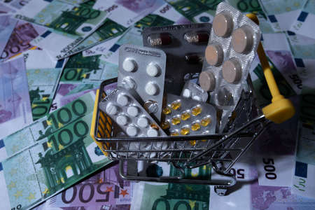 a cart from a supermarket store on a background of money. there are pills and medicine in the cart. small cart abstract background texture background of a billboard or poster dayの写真素材