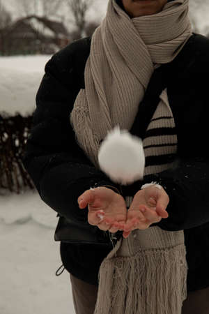a girl in a black jacket and a gray scarf holds a snowball in her hands, crumples it and throws it. snowball on hand snowball gameの写真素材