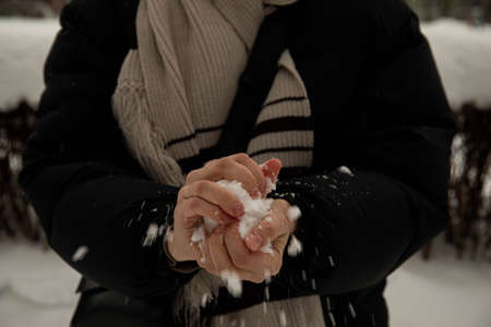 a girl in a black jacket and a gray scarf holds a snowball in her hands, crumples it and throws it. snowball on hand snowball gameの写真素材