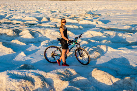 A strong blonde woman in sunglasses stands near a bicycle in a desert area. Fitness concept.の写真素材