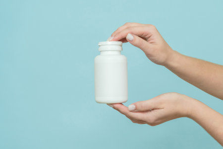 Woman's hand holds a white plastic tube. Bottle for pill, capsule or supplement. Product branding mockupの写真素材