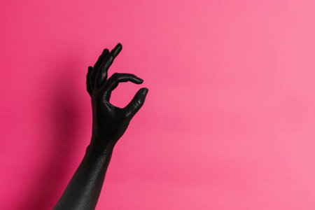Black painted elegant woman's hand on her skin gesticulates on a pink background. High Fashion art conceptの写真素材