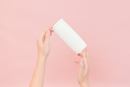 Shampoo, hair conditioner or body lotion bottle in hands in a pink background. Cosmetics bottleの写真素材