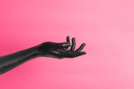 Black painted elegant woman's hand on her skin gesticulates on a pink background. High Fashion art conceptの写真素材