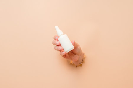 White bottle with serum lotion or essential oil (hyaluronic acid and collagen) in a hand on beige background. Skin care cosmetics concept, beauty flyerの写真素材