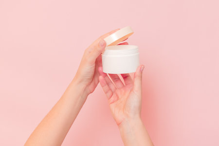 Round jar of cosmetic cream in hand on pink background. Cosmetics beauty mockup for product brandingの写真素材