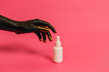 Black and gold painted elegant hand on skin with a cosmetic unbranded bottle. Luxury, high fashion cosmetic products conceptの写真素材