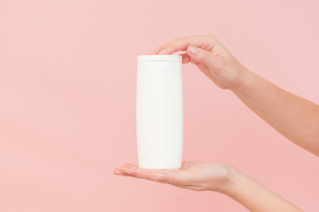 Shampoo, hair conditioner or body lotion bottle in hands in a pink background. Cosmetics bottleの写真素材