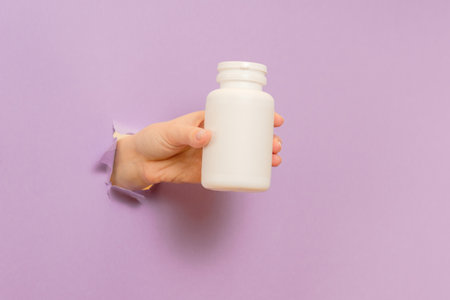 Cool view on white bottle plastic tube in hands on a lilac background. Packaging for pills, capsules or supplements. Cosmeticsの写真素材