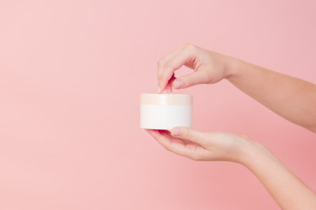 Hand holding jar of cosmetic cream on a pink background. Cosmetics beauty mockup for product brandingの写真素材