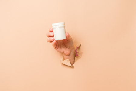 Cool view on white bottle plastic tube in hands on a beige background. Packaging for pills, capsules, supplements or ointment. Cosmeticsの写真素材