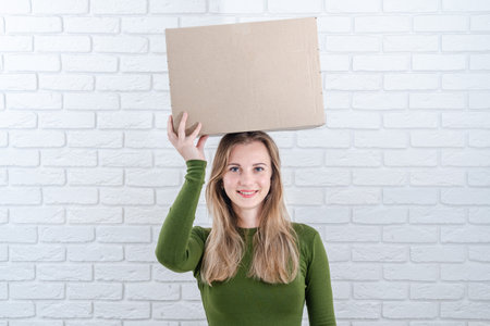 Attractive woman holding parcel box on head. Delivering a parcelの写真素材