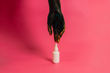 Elegant hand with black and gold paint on skin with a cosmetic unbranded bottle. Luxury, high fashion cosmetic product cosmetic advertisingの写真素材