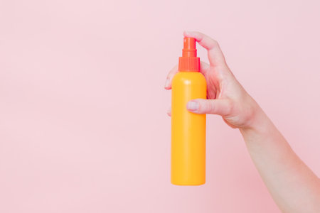 Hand holding plastic spray bottle (as mineral spray or hair spray) on a pink background. Cosmetics beauty mockup for product brandingの写真素材
