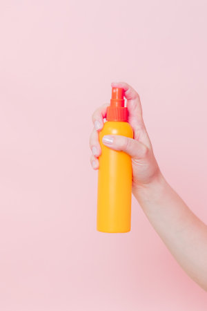 Hand holding plastic spray bottle (as mineral spray or hair spray) on a pink background. Cosmetics beauty mockup for product brandingの写真素材