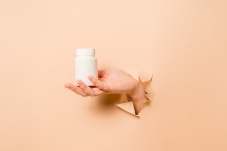 Cool view on white bottle plastic tube in hands on a beige background. Packaging for pills, capsules, supplements or ointment. Cosmeticsの写真素材