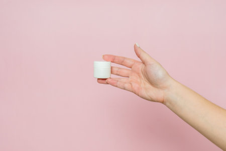 White jar or tube with cream (ointment) in a hand. Facial care, bottle with cosmetic product without labeling.の写真素材