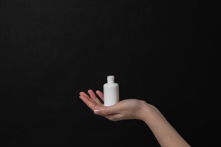 Hand holding serum glass bottle or essential oil with pipette on a black background. Natural Organic...