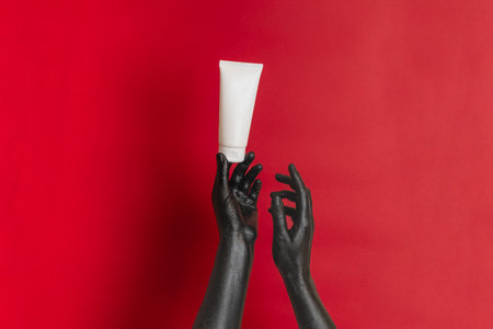 Black painted elegant hands on her skin with a moisturizer cosmetic blank tube. Luxury product cosmetic advertising. Image for your designの写真素材