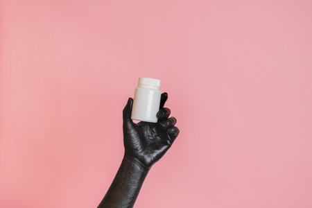 Black painted elegant woman's hand on her skin with a white cosmetic bottle. High Fashion art concept. Product cosmetic advertisingの写真素材