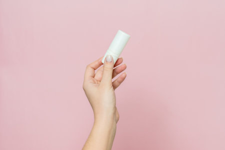 Hand holding white bottle. Drops for eye, nose or ear in hand on a pink background. Pharmaceutical product.の写真素材