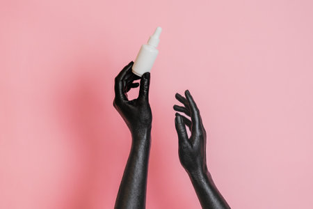 Black painted elegant woman's hands on her skin with a glass cosmetic bottle. Presenting luxury, fashion skincare productsの写真素材