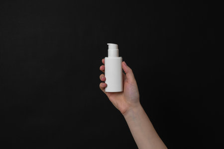 White cosmetic cream tube in hand on a black background. Presenting luxury skincare products.の写真素材