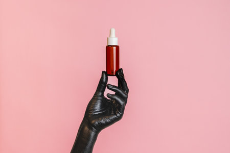 Brown glass bottle with a black painted elegant woman's hand on her skin. Presenting luxury, fashion skincare productsの写真素材