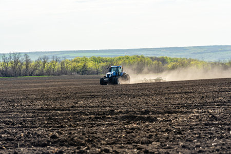 A blue tractor works on a field on a spring morning.の写真素材