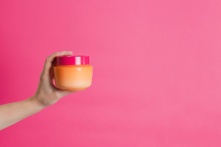Cosmetic bottle for cream, mask or lotion on a hand with pink background. cosmetics for skin, beauty...