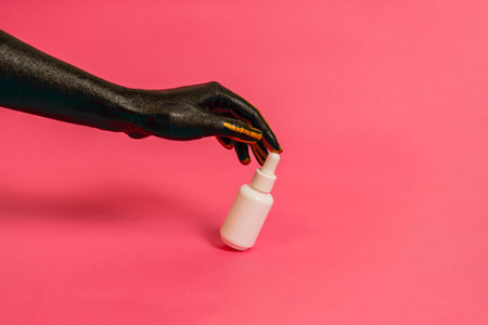 Elegant hand with black and gold paint on skin with a cosmetic unbranded bottle. Luxury, high fashion cosmetic product cosmetic advertisingの写真素材