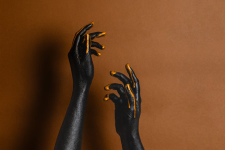 Elegant woman's hands with black and gold painted on her skin on a brown background. High Fashion art conceptの写真素材