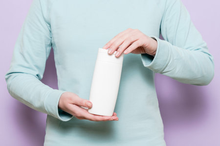 Woman's hand holding packaging of shampoo or conditioner, location. Cosmetic product in a bottle