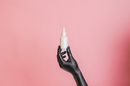 Black painted elegant woman's hand on her skin with a glass cosmetic bottle. Presenting luxury, fashion skincare productsの写真素材
