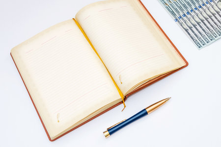 Notebook with pen and dollar banknotes on white background, business conceptの写真素材