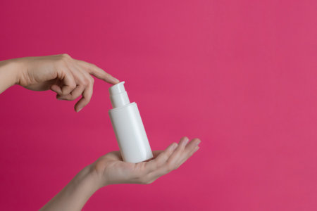 White unbranded cream bottle with pump in hand on a pink background. Natural moisturizing, nourishing cosmetics for skin, beauty and spaの写真素材