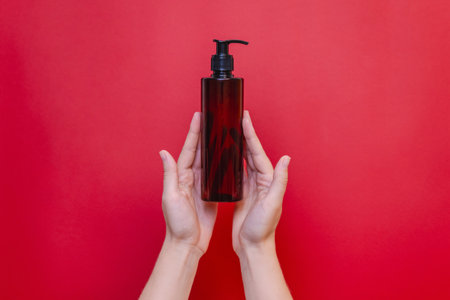 Elegant hand holding blank bottle mockup isolated on the solid red background. Package for cosmetics product, your brand, spa, beauty and luxury. Space for textの写真素材