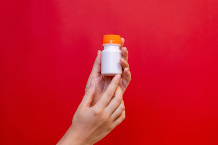 Hand with blank bottle mockup on the red background. Package for cosmetics product, nutritional supplements, vitamins, spa, beauty and luxury. Space for textの写真素材