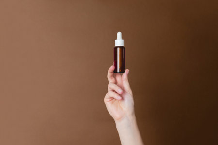 Hand holding serum glass bottle or essential oil on a brown background. Natural Organic Spa Cosmetic conceptの写真素材