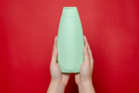 Hand with shampoo light bottle isolated on the solid red background. Package for cosmetics product, your brand, spa, beauty. Space for textの写真素材
