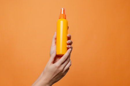 Hand holding a orange spray cosmetic bottle on the solid orange background. Package, your brand