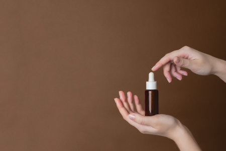 Hand holding serum glass bottle or essential oil on a brown background. Natural Organic Spa Cosmetic conceptの写真素材