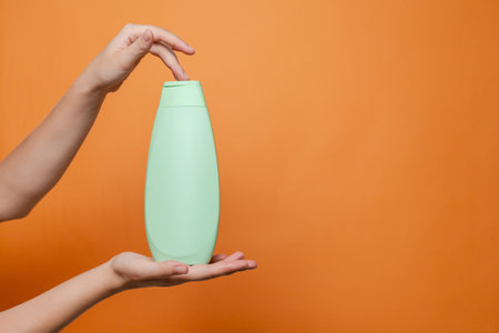 Hand holding shampoo light bottle isolated on the solid orange background. Package for cosmetics product, your brand, spa, beauty. Space for textの写真素材