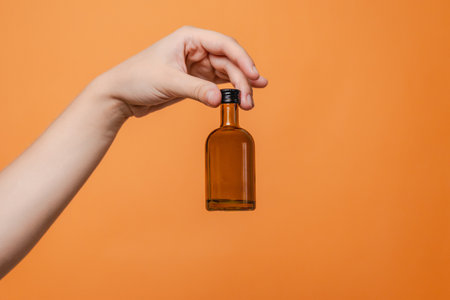 Elegant hand holding small glass blank bottle mockup on the orange background. Package for cosmetics...