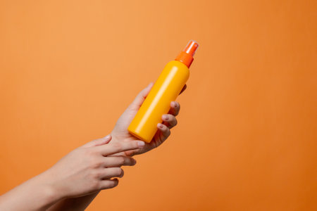 Hand holding a orange spray cosmetic bottle on the solid orange background. Package, your brand